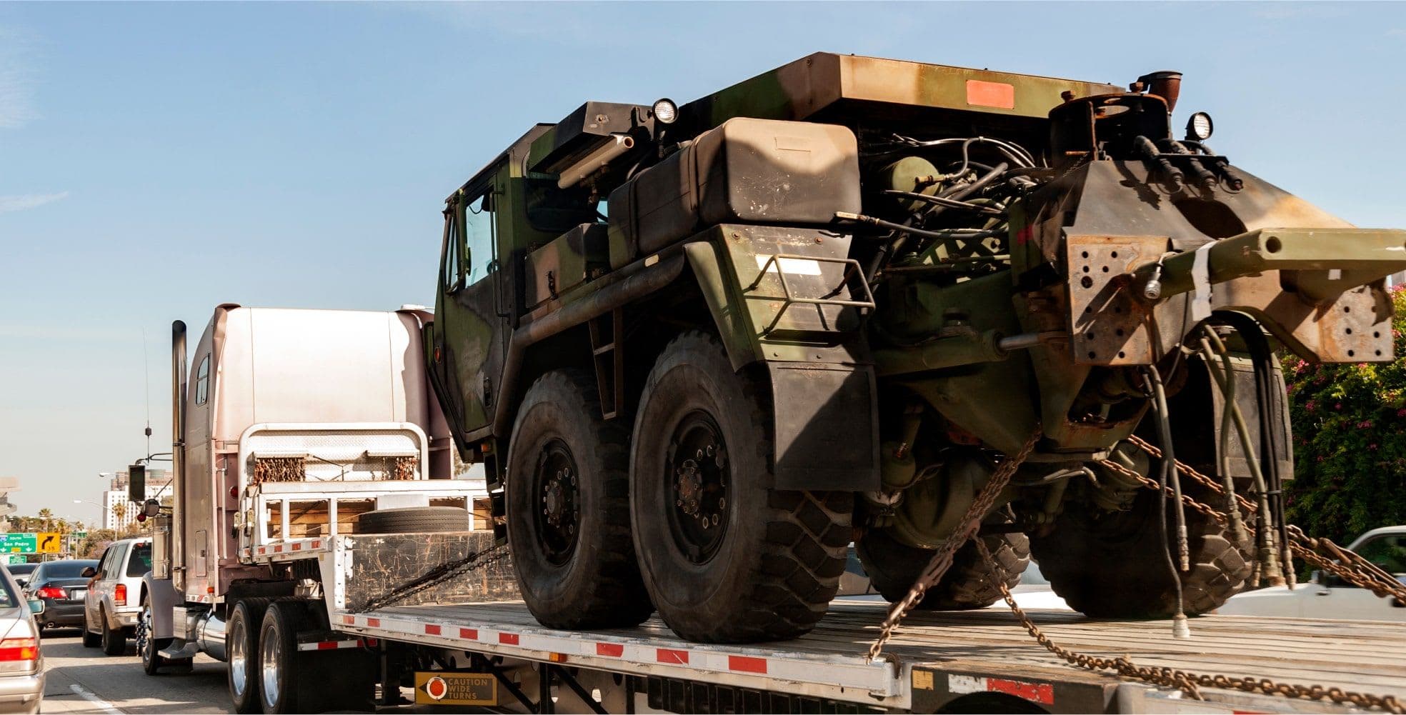 Wize Load Truck driving on interstate hauling a military vehicle.
